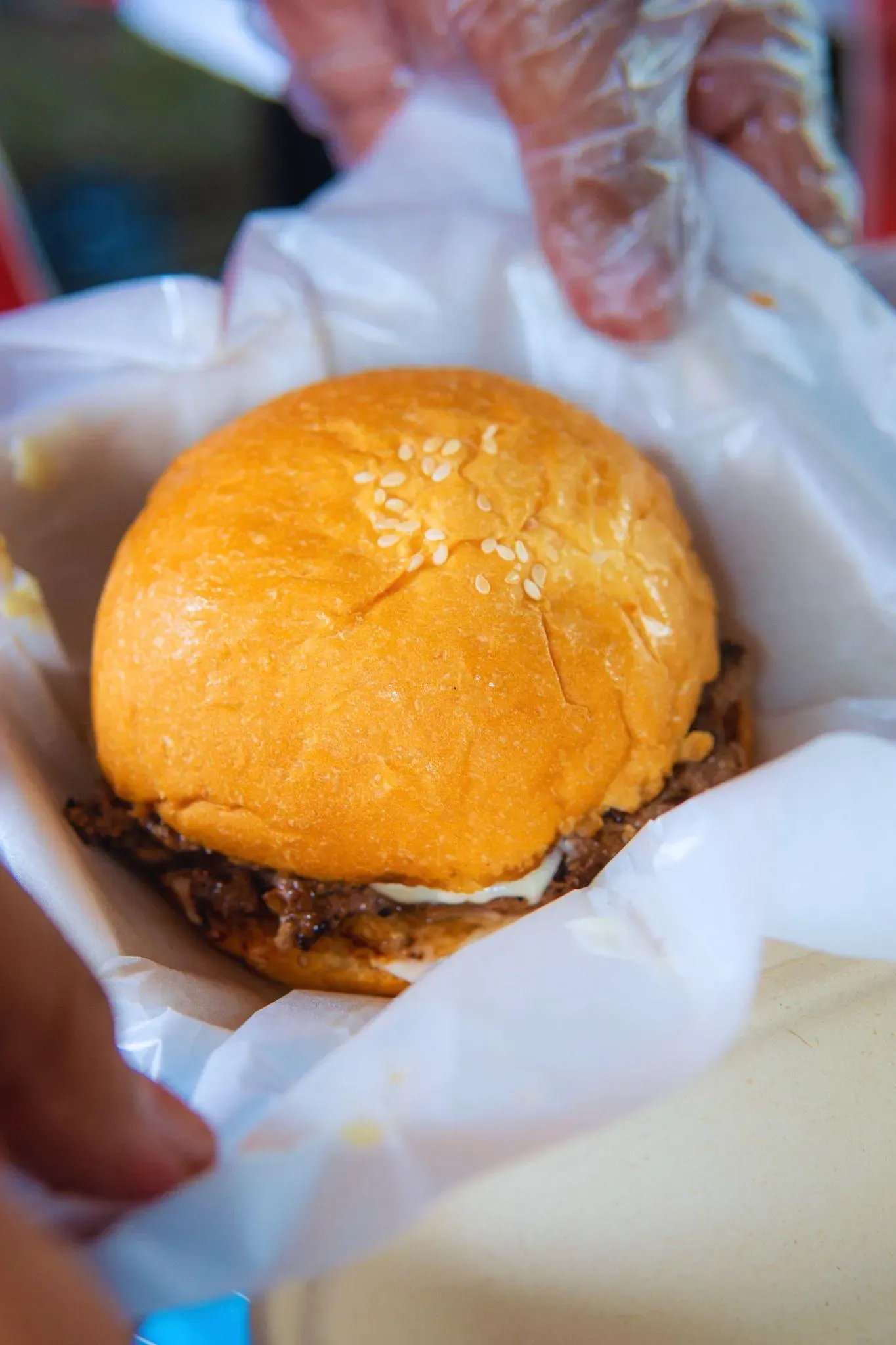 Burger Jaya Abadi dalam kertas pembungkus, dipegang tangan bersarung plastik